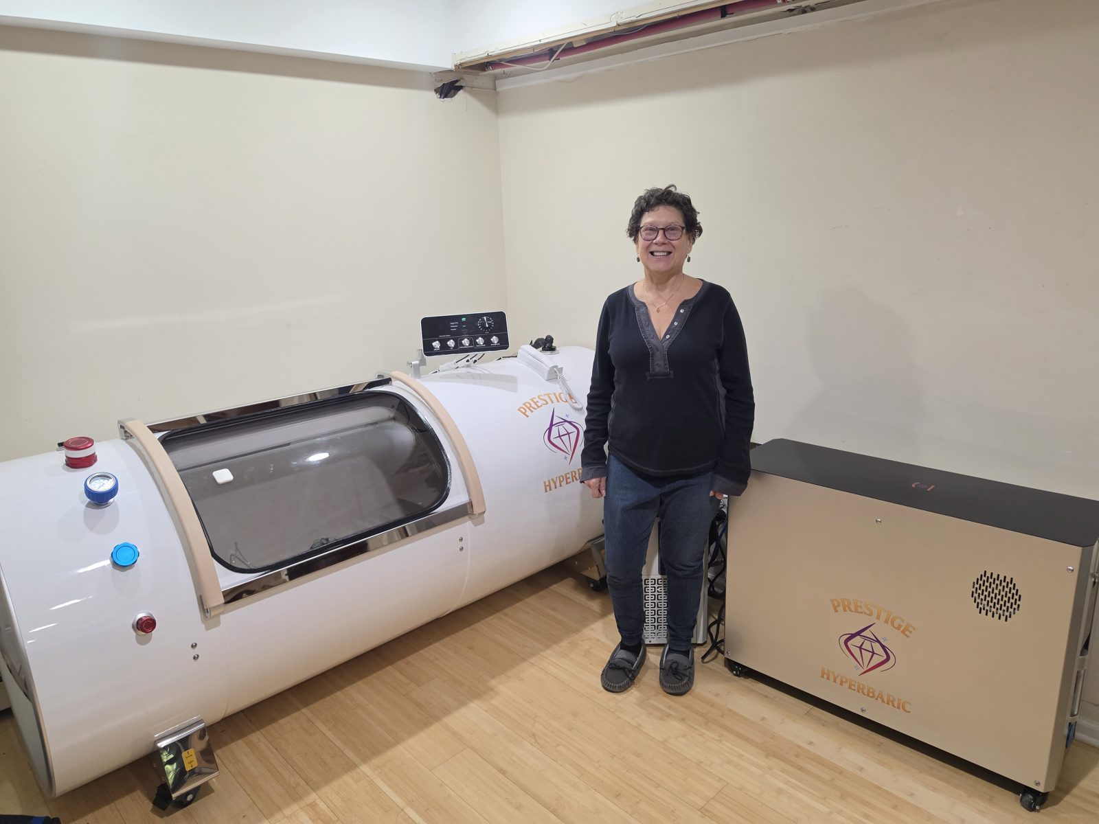 Amy standing beside her Grand Vessel of Power 2.0 ATA hardshell chamber in her New York basement